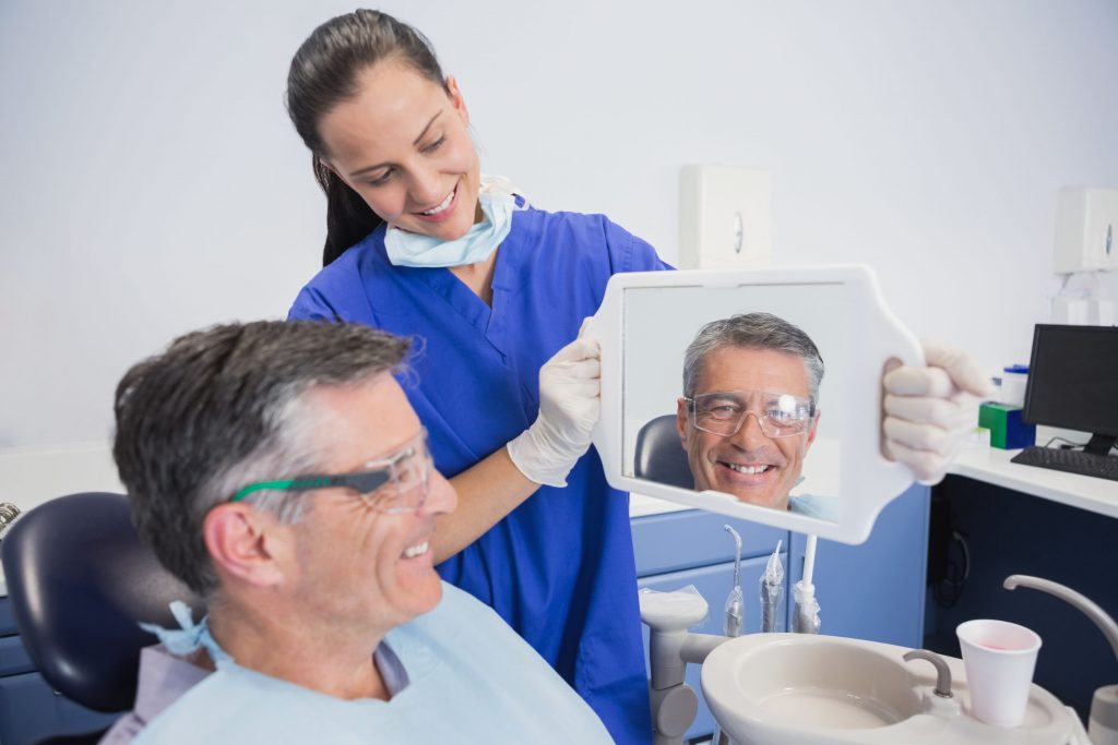 Smiling dentist showing teeth of her patient with a mirror in dental clinic